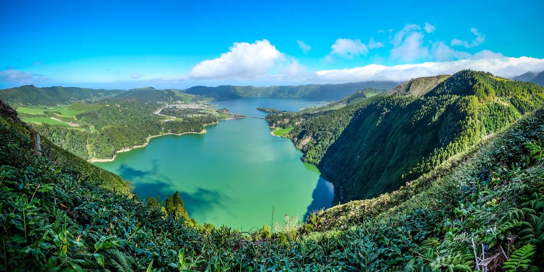 Aerial view of a green crater lake ringed by forested hills