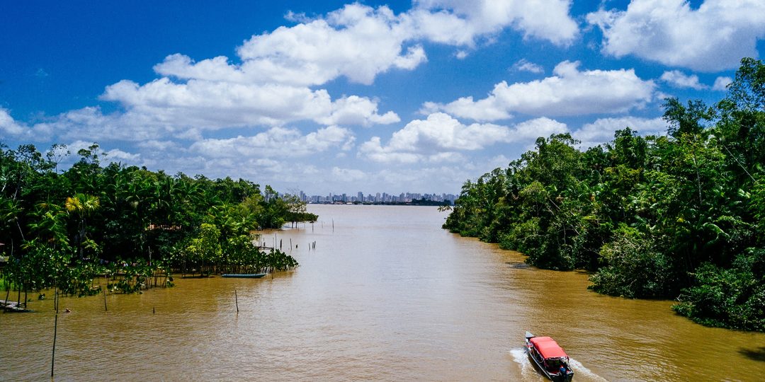 Boat traveling down a wide river through dense rainforest