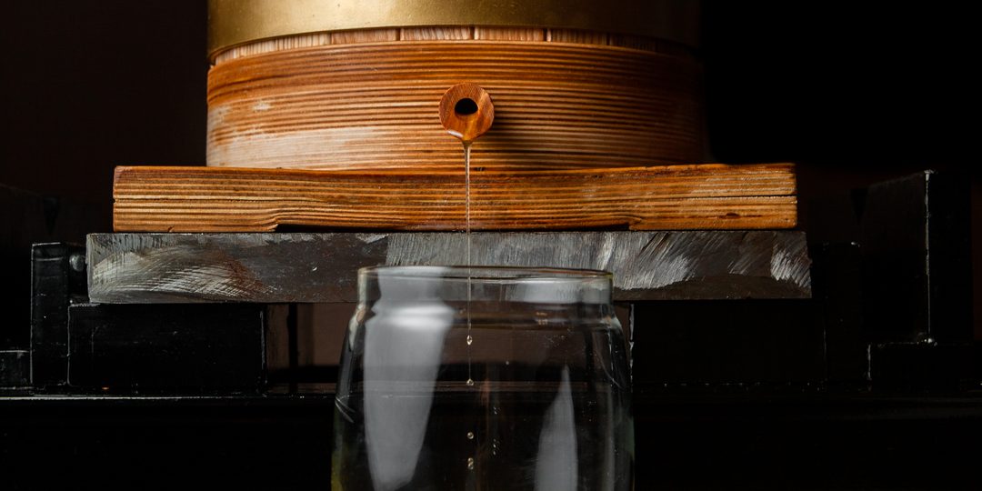 Oil dripping from a wooden press into a glass jar