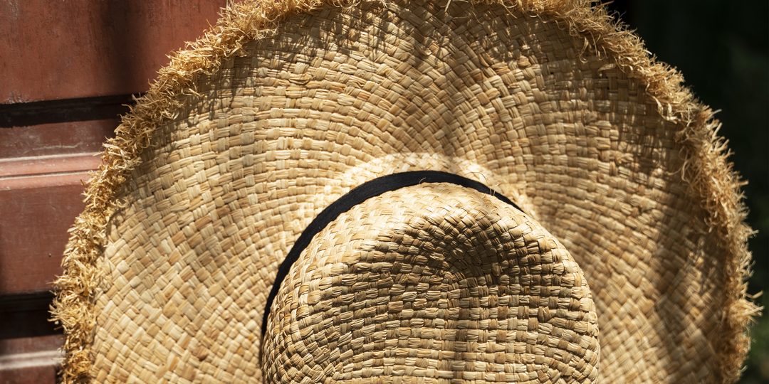 A woven straw hat with a frayed brim hanging against a wooden door