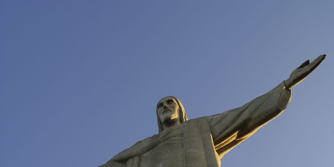 The Christ the Redeemer statue with arms outstretched against a clear blue sky above Rio de Janeiro.