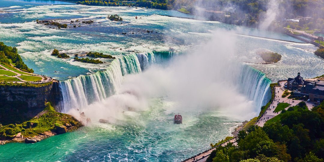Aerial view of Horseshoe Falls at Niagara Falls, with mist rising and a tour boat approaching the base.