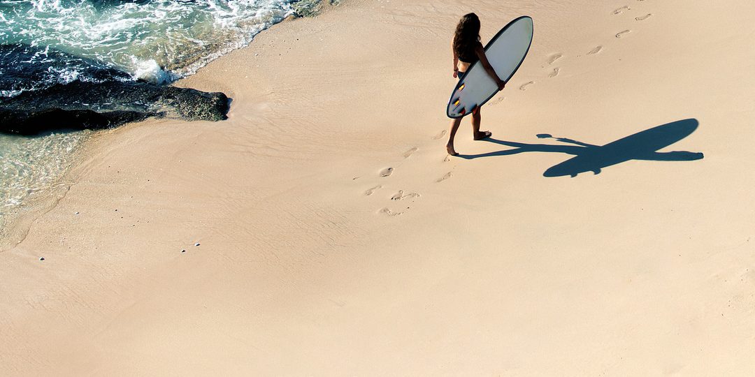 Aerial view of a surfer walking along the shoreline with surfboard in hand