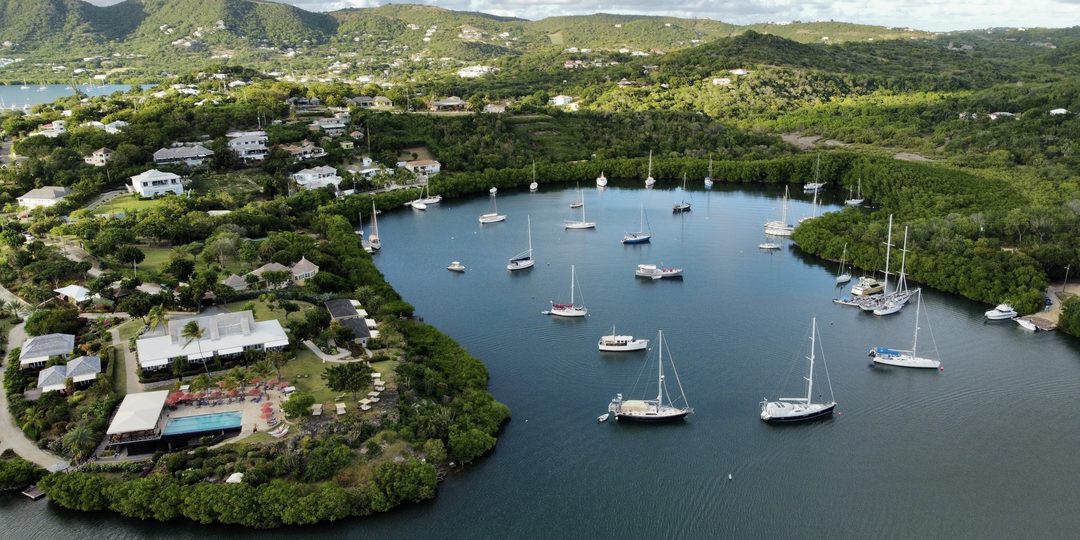 Sailboats anchored in a calm, tree-lined bay