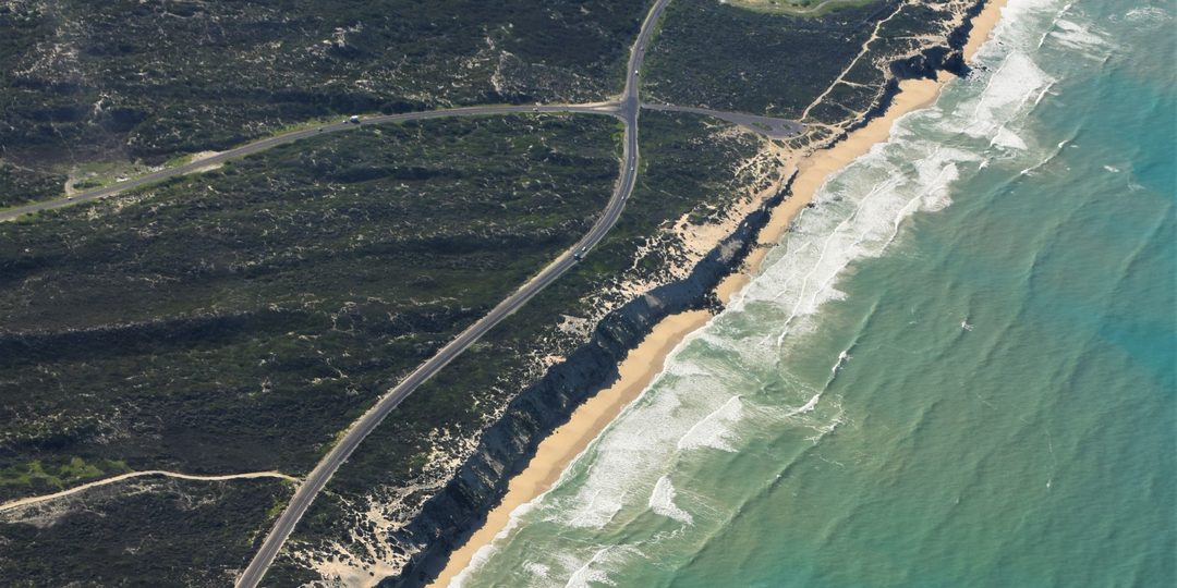 Aerial view of a coastal road winding along cliffs and beach